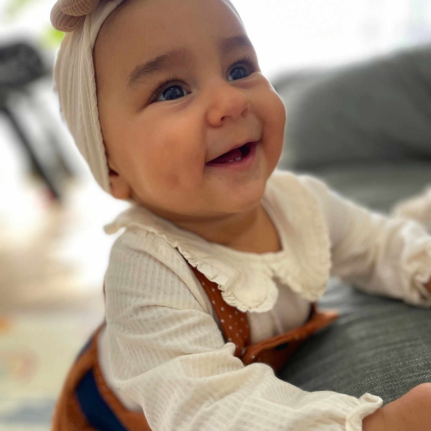 Amélia participe au concours pour gagner de l'argent avec cette photo : baby, bow, brown_overalls, cheeks, child, closeup, couch, cute, eyes, face, happy, headband, homedecor, indoor, infant, person, portrait, smiling, soft_lighting, white_clothing