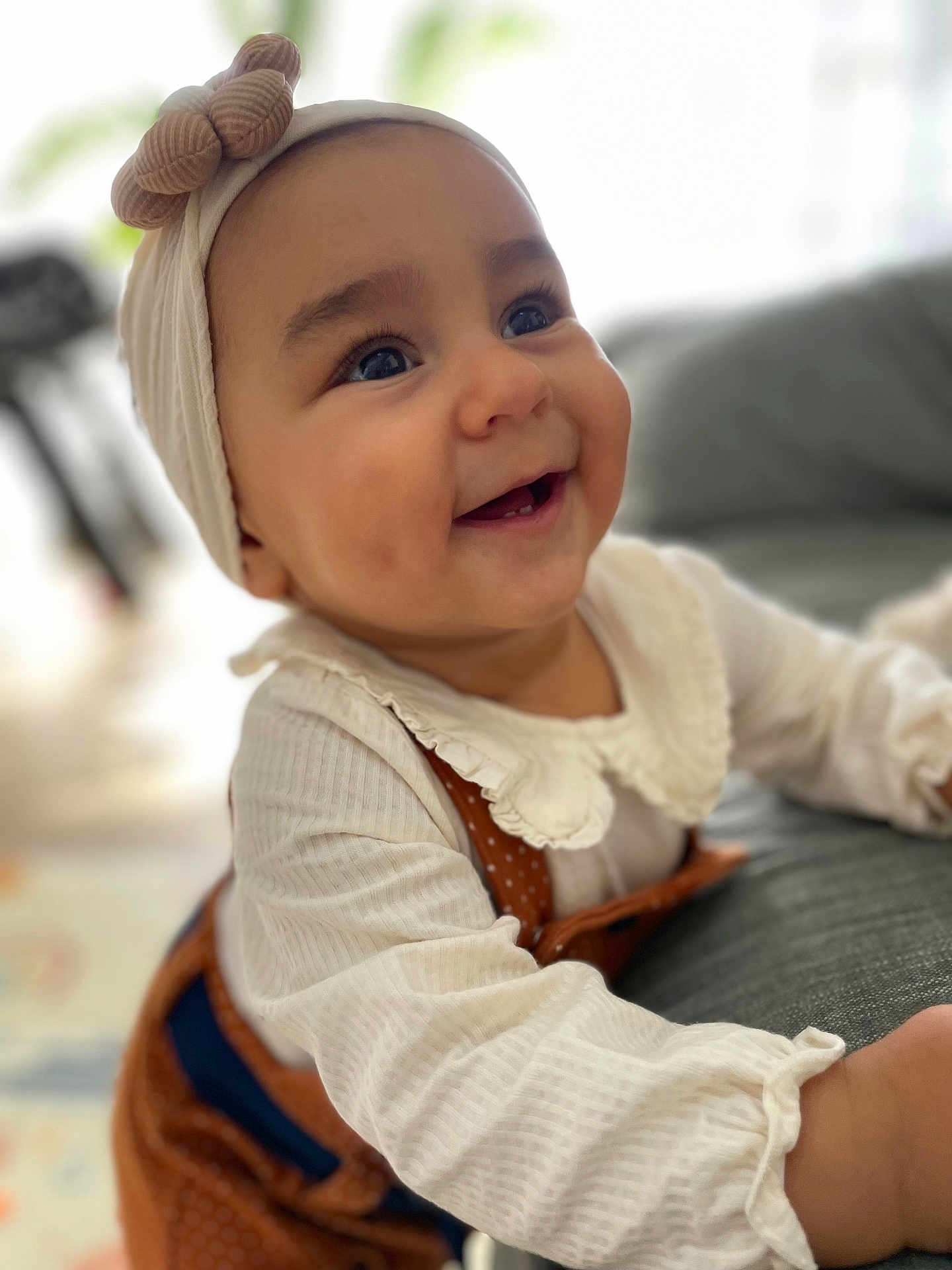 Amélia participe au concours pour gagner de l'argent avec cette photo : baby, child, smiling, headband, bow, white_clothing, brown_overalls, face, eyes, cheeks, infant, couch, indoor, portrait, happy, cute, closeup, person, homedecor, soft_lighting