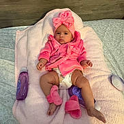 Samantha is registered to the contest to win money with this photo: baby, pink, robe, headwrap, blanket, lotion, slippers, diaper, bed, wooden_headboard, cute, infant, soft_texture, relaxed, indoors, child, person, skin, clothing, laying_down