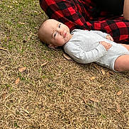 Addilynn is registered to the contest to win money with this photo: baby, infant, onesie, grass, outdoor, person, hand, plaid_pants, red_and_black, side_eye, skeptical_expression, dry_grass, casual_clothing, nature, candid, child, young_child, human, relaxed, daytime