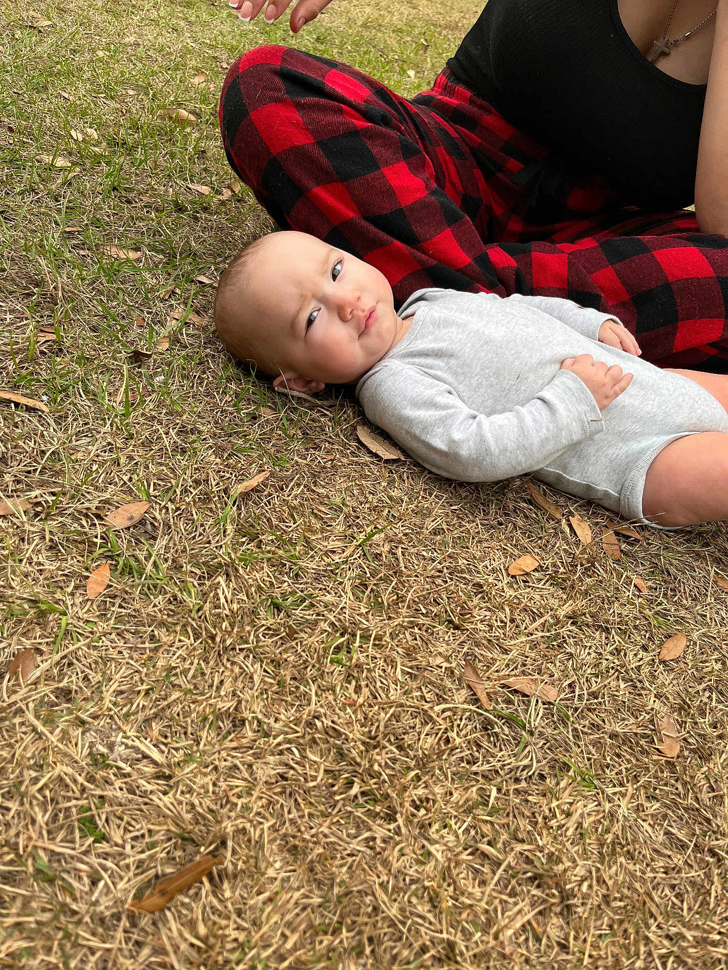 Addilynn is registered to the contest to win money with this photo: baby, infant, onesie, grass, outdoor, person, hand, plaid_pants, red_and_black, side_eye, skeptical_expression, dry_grass, casual_clothing, nature, candid, child, young_child, human, relaxed, daytime