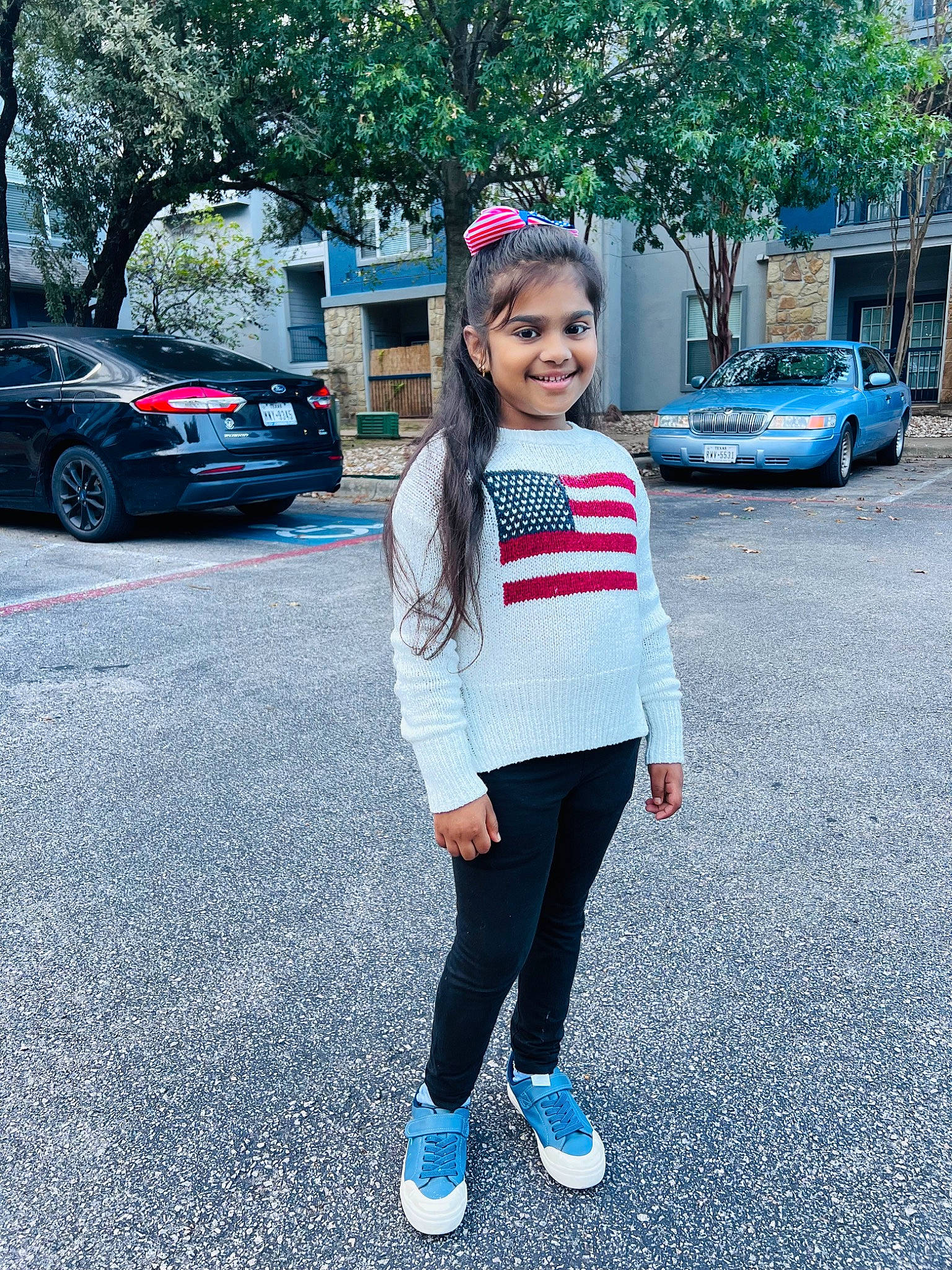 Zara is registered to the contest to win money with this photo: asphalt, automotive_design, automotive_exterior, automotive_lighting, car, footwear, jeans, joy, land_vehicle, leg, motor_vehicle, person, public_space, road_surface, sidewalk, smile, standing, tire, tree, vehicle