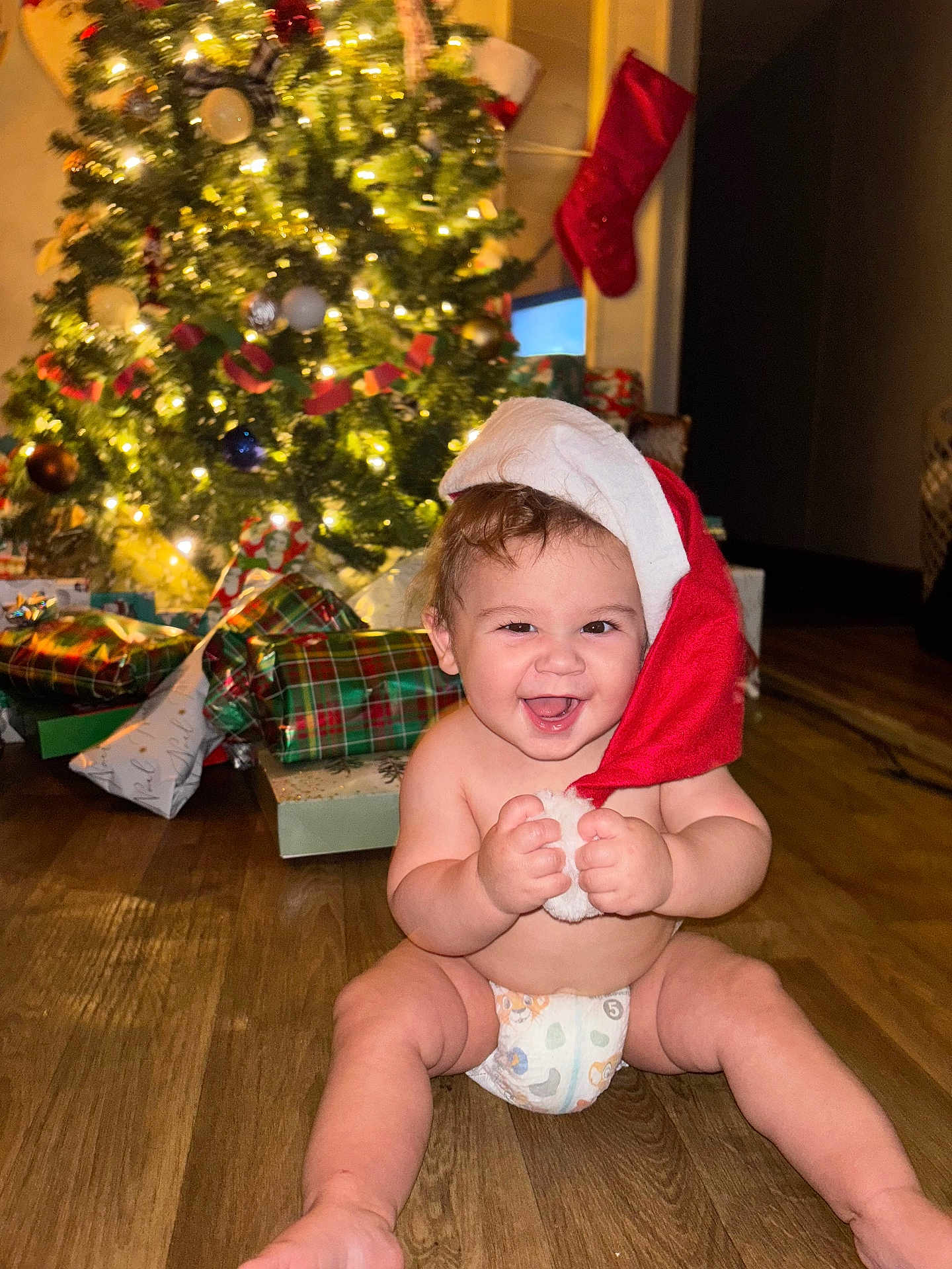 Atlas joined the competition — help win amazing prizes! baby, child, santa_hat, christmas_tree, presents, holiday, festive, smiling, diaper, floor, indoor, happy, cute, celebration, christmas_stocking, decorations, lights, christmas, joy, holiday_season