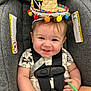 baby, car_seat, smiling, sombrero, hat, infant, child, seatbelt, straps, warning_labels, clothing, hand, face, cute, sitting, indoor, colorful, cheerful, toy, closeup