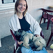 Blue participe au concours pour gagner de l'argent avec cette photo : woman, dog, smile, chair, outdoor, casual, jeans, pet, happy, relaxed, daylight, building, window, poster, fur, animal, seated, pavement, plastic_chair, friendship