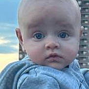 Roberto Candelatia is registered to the contest to win money with this photo: apartment_building, baby, blue_eyes, child, close_up, daylight, expression, face, gray_clothing, infant, outdoor, person, photograph, portrait, sitting, sky, sunset, sweatshirt, urban, wide_eyed