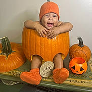 Arya is registered to the contest to win money with this photo: baby, pumpkin, orange, hat, socks, table, carved_pumpkin, smiling, six_months, decor, halloween, child, festive, cute, indoor, person, holiday, seasonal, pumpkin_bucket, happy