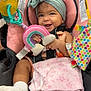 baby, child, smiling, headband, toy, car_seat, blanket, sock, indoors, cute, happy, infant, colorful, pink, gray, holding, seat, playful, portrait, childcare