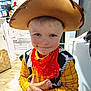 appliance, boy, cabinet, child, costume, cowboy_hat, door, face, hand, indoor, kitchen, light, person, playful, portrait, red_bandana, smile, wood_floor, yellow_shirt, young