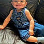 baby, child, smiling, denim_overalls, blue_shirt, leather_couch, happy, sitting, indoor, cute, infant, portrait, person, skin, face, hand, foot, clothing, young, casual