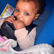 Xaya is registered to the contest to win money with this photo: baby, child, curly_hair, car_seat, blanket, blue, buckle, chewing, cute, infant, hand, eyes, clothing, seatbelt, indoors, portrait, person, closeup, sitting, young
