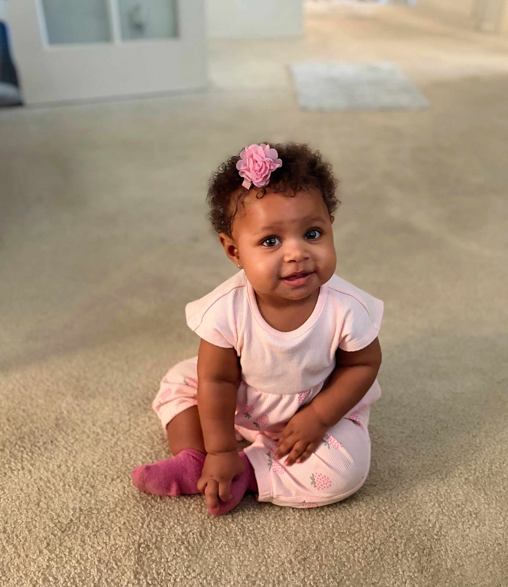 Xaya joined the competition — help win amazing prizes! child, baby, toddler, sitting, pink_outfit, flower_hairclip, curly_hair, smiling, indoor, carpet, sock, portrait, cute, chubby_cheeks, big_eyes, earring, playful, home_interior, soft_lighting, skin_tone