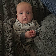 Colt is registered to the contest to win money with this photo: baby, child, infant, portrait, face, sitting, blanket, fleece, cuddly, cozy, gray, clothing, onesie, hands, wide_eyed, indoors, bed, pillow, penguin, spotted_blanket
