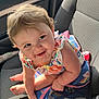 baby, child, car_seat, smiling, curly_hair, colorful_clothing, blue_backpack, rainbow, unicorn, sunlight, happy, cute, infant, seatbelt, car_interior, portrait, sitting, playful, young_child, person