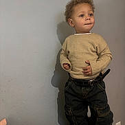 Rylee Rice joined the competition — help win amazing prizes! toddler, child, curly_hair, beige_sweater, dark_jeans, belt, standing, shoes, indoor, wall, shadow, looking_away, casual_clothing, young_child, portrait, person, curious, fashion, cute, light