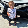 toddler, child, curly_hair, white_tshirt, nike_air, black_shorts, sneakers, red_and_black_shoes, car, white_car, toyota_logo, outdoor, concrete, shadow, daylight, standing, person, cute, sunlight, portrait