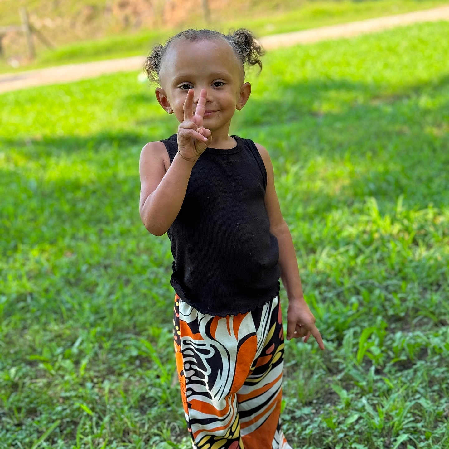 Kinslee joined the competition — help win amazing prizes! black_tank_top, casual_clothing, child, colorful_pants, curly_hair, daytime, grass, greenery, happy, nature, outdoor, peace_sign, person, pigtails, playful, portrait, smiling, standing, sunlight, young_child