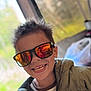 child, smiling, sunglasses, reflection, face, hair, jacket, clothing, indoor, window, blurred_background, person, portrait, happy, casual, playful, teeth, headshot, eyewear, reflection_glasses