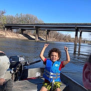 Shawn joined the competition — help win amazing prizes! child, boy, life_vest, boat, river, bridge, water, outdoor, nature, trees, sky, summer, smiling, happy, casual_clothing, curly_hair, adventure, recreation, sunny, daytime