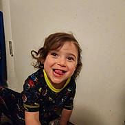 Elora joined the competition — help win amazing prizes! toddler, child, curly_hair, smiling, tongue_out, space_outfit, indoor, floor, wall, playful, happy, person, clothing, young_child, cute, expression, sitting, toy, casual, portrait