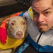 Noel O joined the competition — help win amazing prizes! man, dog, yellow_sweater, selfie, indoor, brown_dog, facial_hair, braided_hair, colorful_jacket, black_pants, blue_bear_designs, wooden_floor, floral_fabric, close_up, pet, companion, casual_clothing, portrait, warm_lighting, calm_expression
