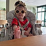 Tyanna participe au concours pour gagner de l'argent avec cette photo : toddler, child, sunglasses, headband, high_chair, foot, red_shirt, indoor, table, person, baby, hair, seatbelt, furniture, window, light, playful, expression, room, casual