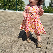 Tyanna a rejoint le concours — aidez-le/la à gagner de superbes lots ! toddler, child, girl, smiling, walking, floral_dress, curly_hair, outdoor, sunny, pavement, greenery, railing, happy, young_child, casual_clothing, daylight, shoes, shadow, exploring, playful