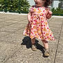 casual_clothing, child, curly_hair, daylight, exploring, floral_dress, girl, greenery, happy, outdoor, pavement, playful, railing, shadow, shoes, smiling, sunny, toddler, walking, young_child