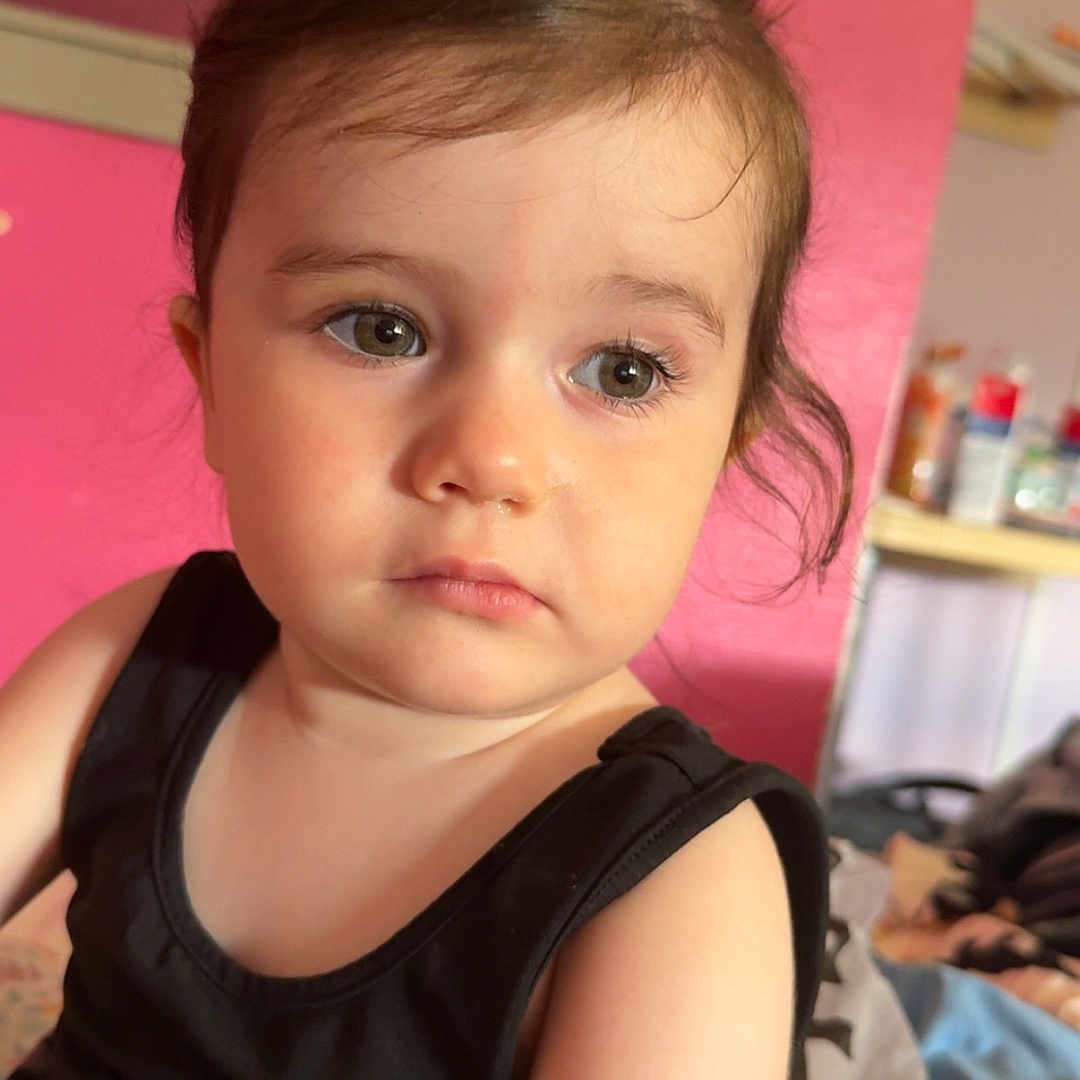 Tyanna a rejoint le concours — aidez-le/la à gagner de superbes lots ! black_tank_top, blanket, casual, child, clothing, curly_hair, expression, eyes, face, head, household_items, indoor, looking_away, person, pink_wall, portrait, shelf, skin, toddler, young_child