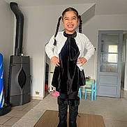 Jane participe au concours pour gagner de l'argent avec cette photo : child, girl, smiling, standing, pigtails, black_dress, white_cardigan, boots, indoor, table, carpet, door, kids_table, chair, soccer_ball, floor, stove, home, happy, portrait