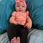 Delilah joined the competition — help win amazing prizes! baby, infant, bow_headband, pink_clothing, onesie, teal_pillow, pillow, bed, blanket, legs, toes, hands, blue_eyes, face, portrait, sitting, cute, indoors, fabric, smile