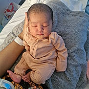Sara is registered to the contest to win money with this photo: baby, newborn, sleeping, infant, hand, blanket, onesie, cozy, soft, peaceful, resting, bed, adult_hand, skin, foot, toe, clothing, portrait, indoors, closeup