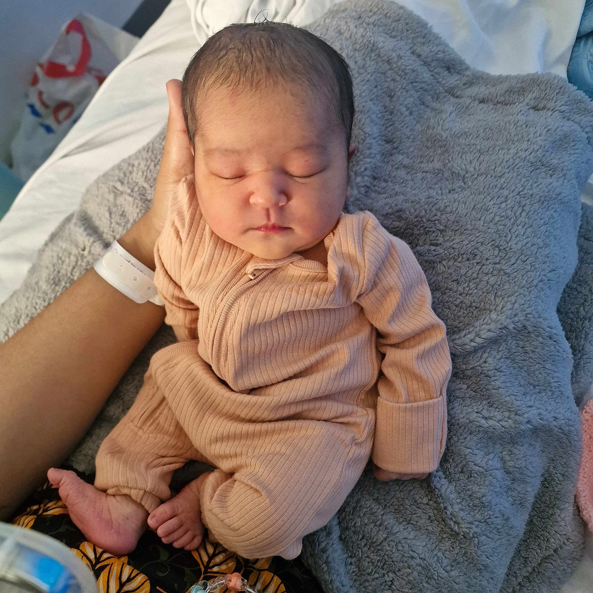 Sara is registered to the contest to win money with this photo: baby, newborn, sleeping, infant, hand, blanket, onesie, cozy, soft, peaceful, resting, bed, adult_hand, skin, foot, toe, clothing, portrait, indoors, closeup