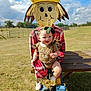 baby, child, scarecrow, outdoor, grass, blue_sky, clouds, plaid_shirt, headband, smiling, table, wood, field, sunny, person, toy, cute, green, footwear, nature