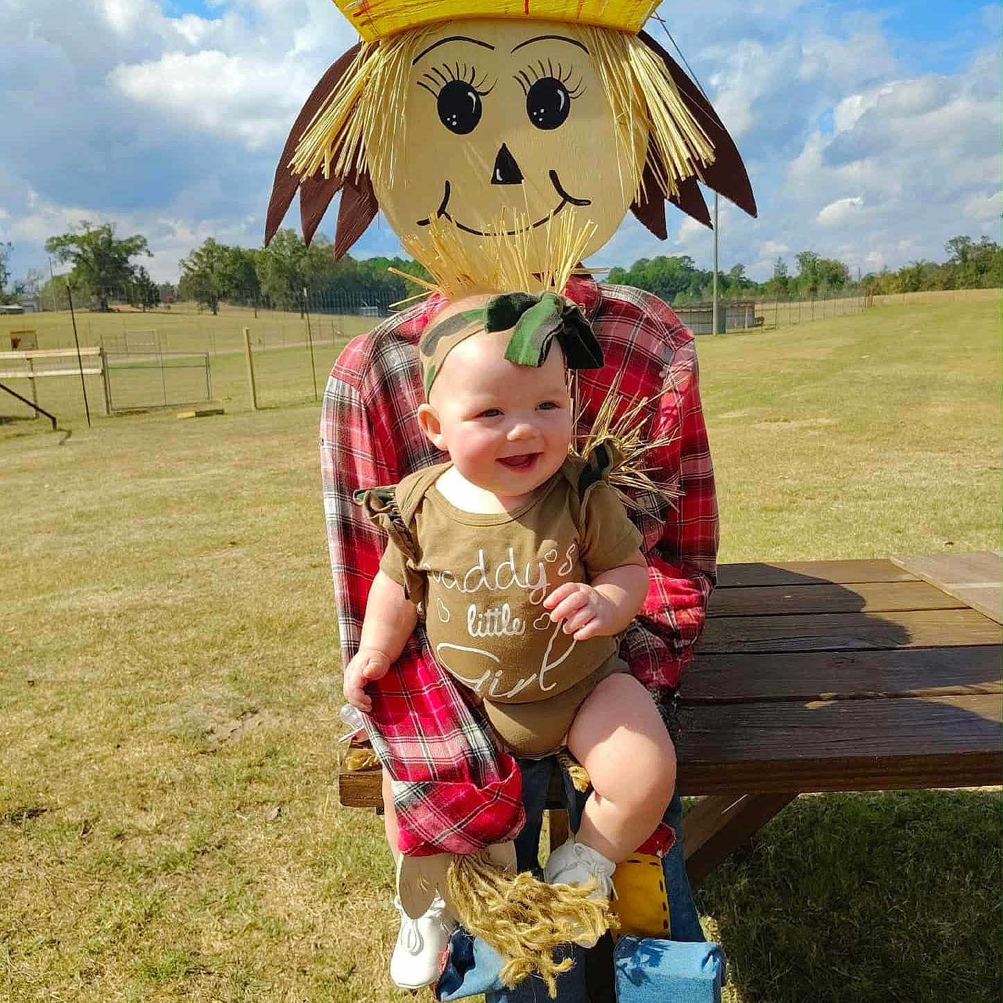Nellie joined the competition — help win amazing prizes! baby, blue_sky, child, clouds, cute, field, footwear, grass, green, headband, nature, outdoor, person, plaid_shirt, scarecrow, smiling, sunny, table, toy, wood
