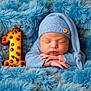 newborn, baby, sleeping, blue, knit_hat, blanket, cookie, number_one, cute, resting, infant, soft_texture, portrait, cozy, hands, closed_eyes, celebration, milestone, child, peaceful