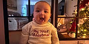 Axel joined the competition — help win amazing prizes! baby, child, infant, sweater, christmas, holiday, christmas_tree, indoors, smiling, happy, home, living_room, furniture, decorations, festive, cute, portrait, seated, warm_lighting, celebration