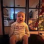 baby, child, infant, sweater, christmas, holiday, christmas_tree, indoors, smiling, happy, home, living_room, furniture, decorations, festive, cute, portrait, seated, warm_lighting, celebration