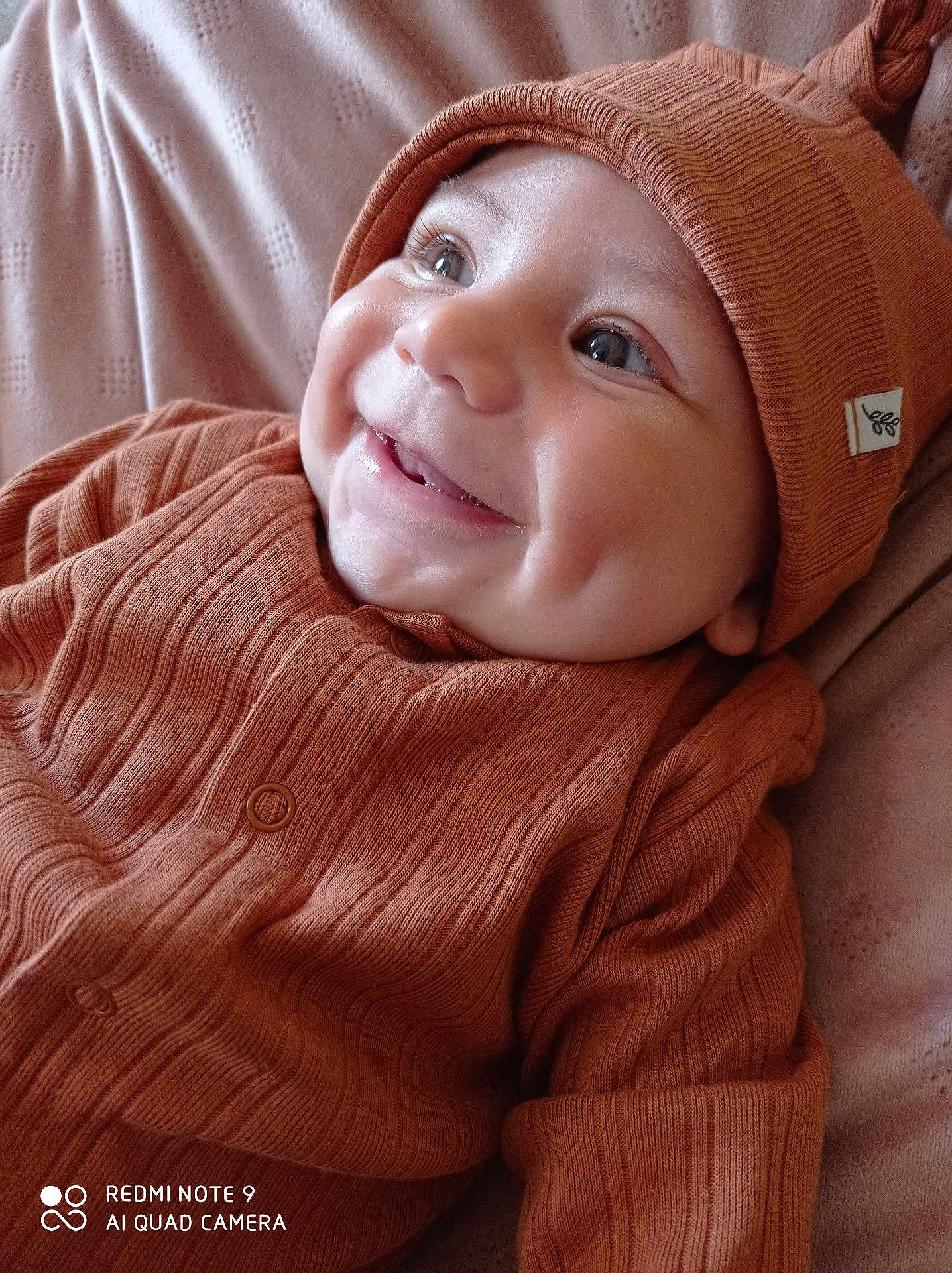 Tiago participe au concours pour gagner de l'argent avec cette photo : baby, infant, smile, dimples, orange_clothing, knit_hat, knitwear, cozy, cute, portrait, happy, child, face, closeup, soft_texture, blanket, indoor, young, person, warm