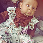 Inaya a rejoint le concours — aidez-le/la à gagner de superbes lots ! baby, child, infant, clothing, outfit, boots, bed, room, photographs, wall, person, sitting, curious, indoor, soft_lighting, cute, pink, brown, patterned, pacifier