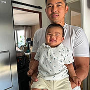 Sak a rejoint le concours — aidez-le/la à gagner de superbes lots ! baby, adult, smile, person, indoor, kitchen, clothing, holding, shorts, shirt, refrigerator, appliance, cabinet, plant, window, curtain, happy, family, portrait, casual