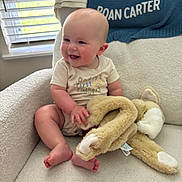 Roan is registered to the contest to win money with this photo: baby, armchair, stuffed_animal, smiling, indoors, window, blanket, child, happy, soft_toys, cozy, natural_light, clothing, person, furniture, cute, infant, home, blinds, sitting