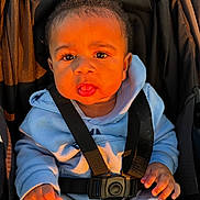 Daniel is registered to the contest to win money with this photo: baby, child, stroller, blue_hoodie, black_straps, curly_hair, cute, infant, seated, sunlight, portrait, face, hands, clothing, casual_wear, outdoor, young_child, expression, warm_light, closeup