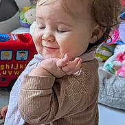 Amelia joined the competition — help win amazing prizes! baby, child, toddler, smile, face, hair, clothing, indoors, toy, playroom, sitting, cute, expression, home, furniture, blanket, person, soft_lighting, happy, portrait