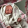 baby, sleeping, knitted_clothing, white_outfit, bunny_ears, blanket, pink_flower_pattern, infant, peaceful, cute, soft_lighting, portrait, closeup, hand, newborn, cozy, indoors, child, face, buttoned_sweater