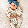 adorable, baby, blue_bow, child, cozy, cute, fashion, floral_outfit, happy, headband, indoors, infant, lying_down, portrait, small_hands, smile, soft_lighting, tights, white_blanket, young