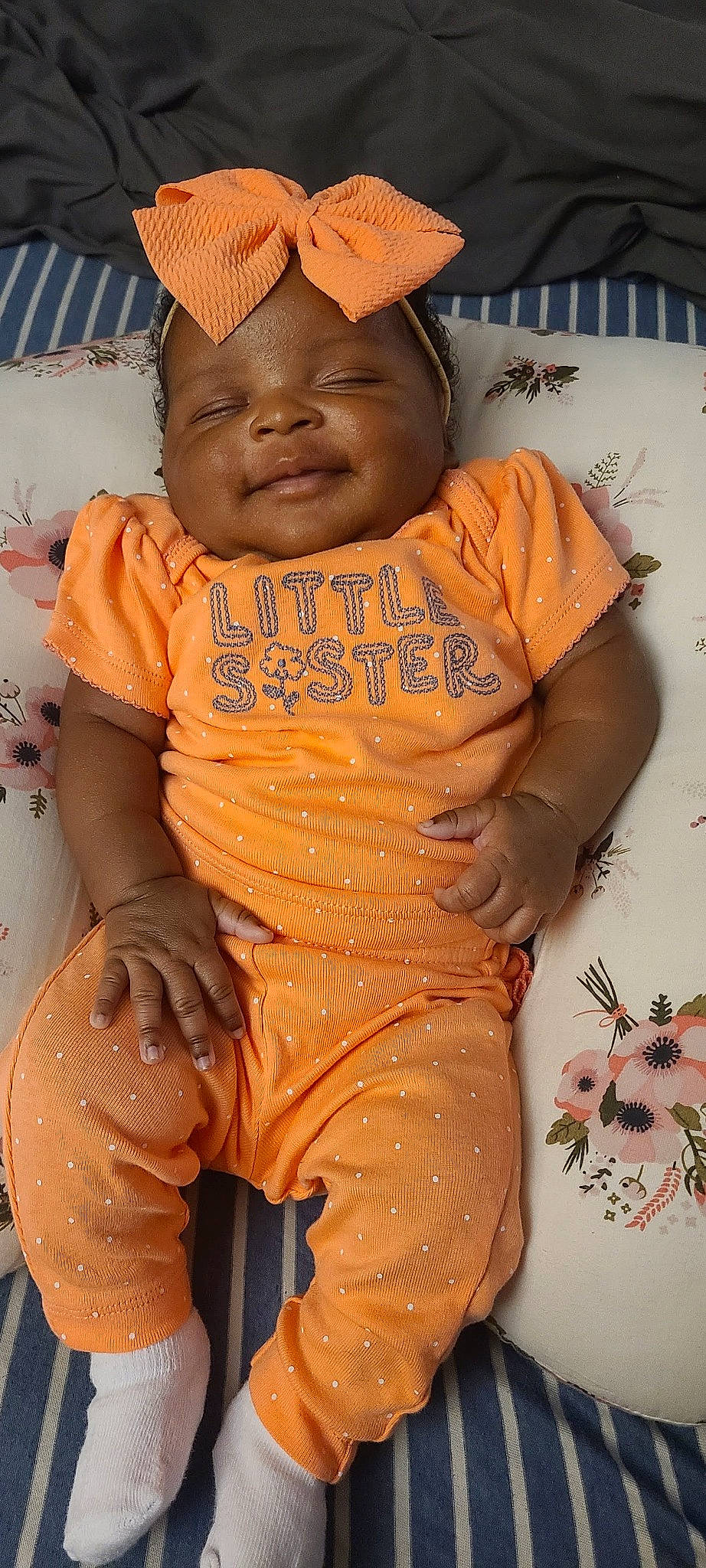 Amirah is registered to the contest to win money with this photo: arm, baby, baby_toddler_clothing, cap, cheek, face, facial_expression, finger, forehead, hand, happy, head, headwear, neck, orange, person, skin, sleeve, smile, t_shirt