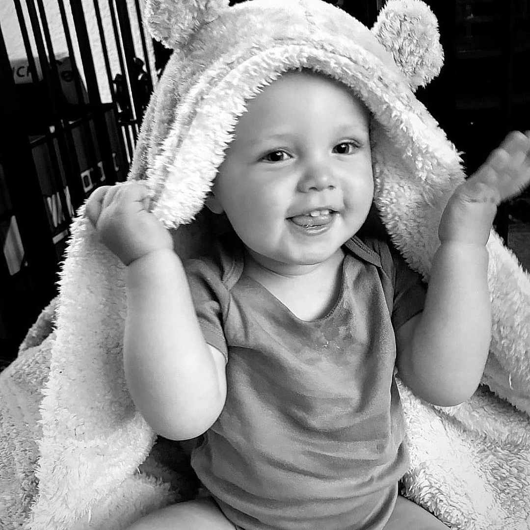 Hunter is registered to the contest to win money with this photo: baby, bodypart, bonnet, cap, clothing, face, finger, furniture, hand, happy, hat, head, person, photography, portrait, shorts, sitting, smile, sunhat, towel