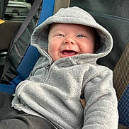 Braxten is registered to the contest to win money with this photo: baby, hoodie, smile, car_seat, blue, black, clothing, child, happy, infant, portrait, seatbelt, cute, casual, sitting, young, face, cozy, warm, indoor