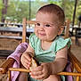 baby, child, high_chair, bread, food, outdoor, table, wooden_chair, greenery, cute, smiling, infant, clothing, person, portrait, happy, seated, daylight, toddler, skin